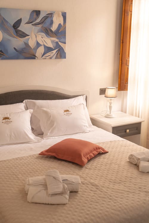 Ampia camera doppia all'hotel Al Cinghiale con biancheria bianca, cuscino d'accento arancione e quadro con foglie sopra il letto