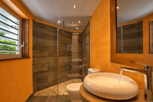 Salle de bains moderne aux murs orange, douche en bois foncé et lavabo blanc épuré de la villa Les Balcons D'Oyster Pond