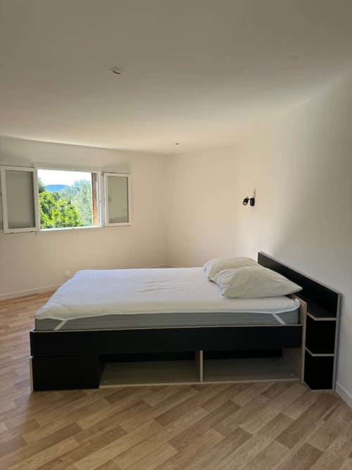 Chambre moderne avec lit plateforme noir, literie blanche, parquet, grande fenêtre donnant sur les montagnes aux Villas d'A