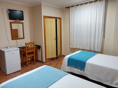 Habitación doble de Hotel La Posada con dos camas individuales, televisor, escritorio, minibar y ventana con cortinas en España