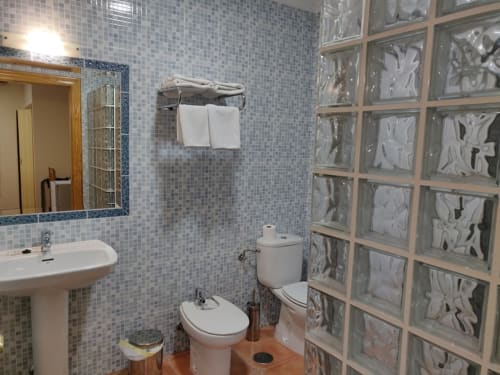 Baño moderno del Hotel La Posada con azulejos de mosaico azul, lavamanos de pedestal, bidé, inodoro y ventana de bloque de vidrio decorativo