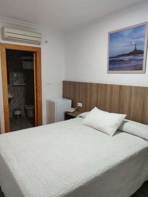 Habitación doble en Hotel La Posada con ropa de cama blanca, cabecera de madera, aire acondicionado y cuadro de faro marino