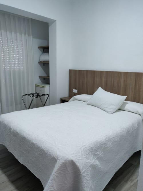 Moderna habitación doble en Hotel La Posada con ropa de cama blanca, cabecera de madera, armario empotrado y decoración minimalista