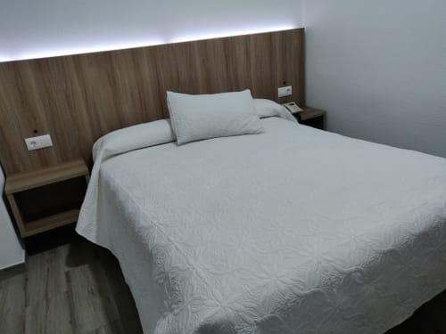 Moderna habitación doble en Hotel La Posada con ropa de cama acolchada blanca, cabecero de madera, iluminación ambiental y diseño contemporáneo