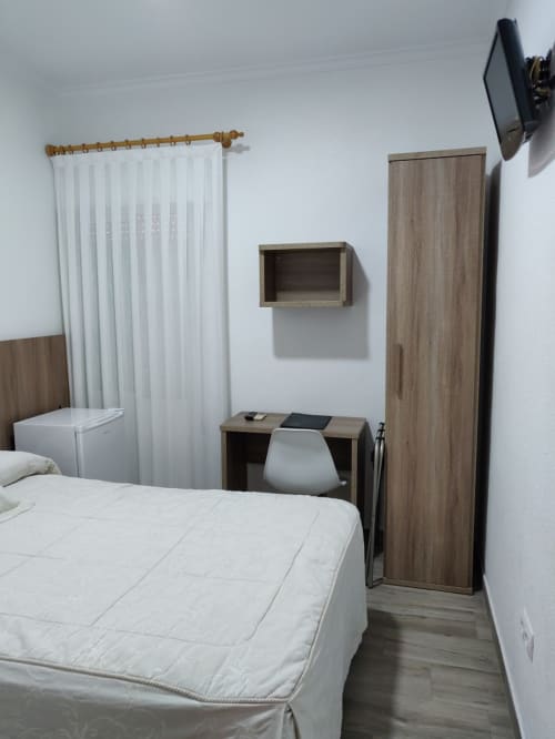 Amplia habitación doble en Hotel La Posada con ropa de cama blanca, muebles de madera, escritorio, TV mural y ventanales