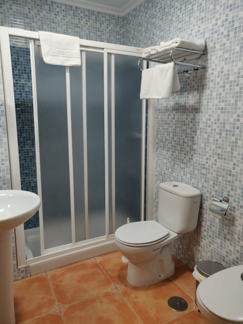 Baño moderno en Hotel La Posada con ducha, inodoro, lavamanos pedestal y paredes con azulejos de mosaico