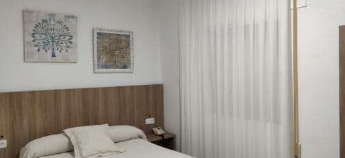 Moderna habitación doble en Hotel La Posada con cabecera de madera, ropa de cama blanca y cuadro de árbol en la pared
