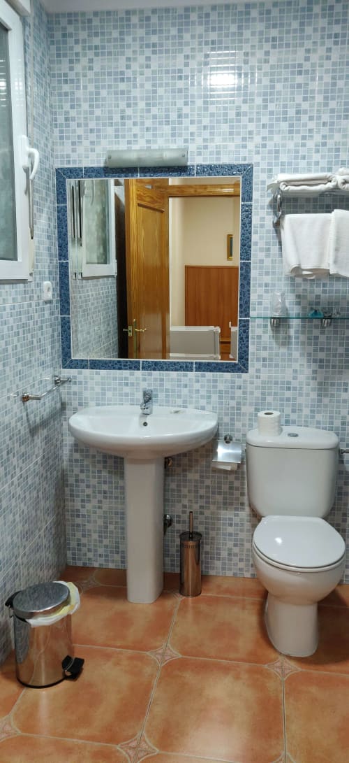 Baño moderno del Hotel La Posada con paredes de azulejos, lavamanos de pedestal, inodoro y espejo enmarcado