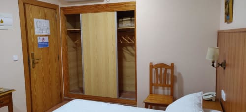 Habitación del Hotel La Posada con camas gemelas, armario de madera y silla en España