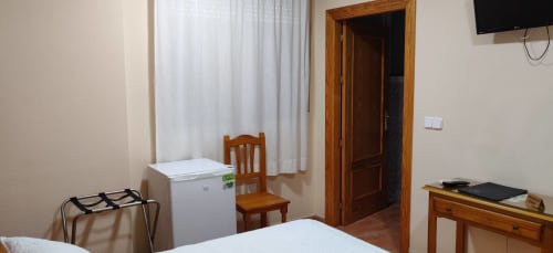 Habitación doble del Hotel La Posada con cama, minibar, muebles de madera, TV y cortinas blancas en España