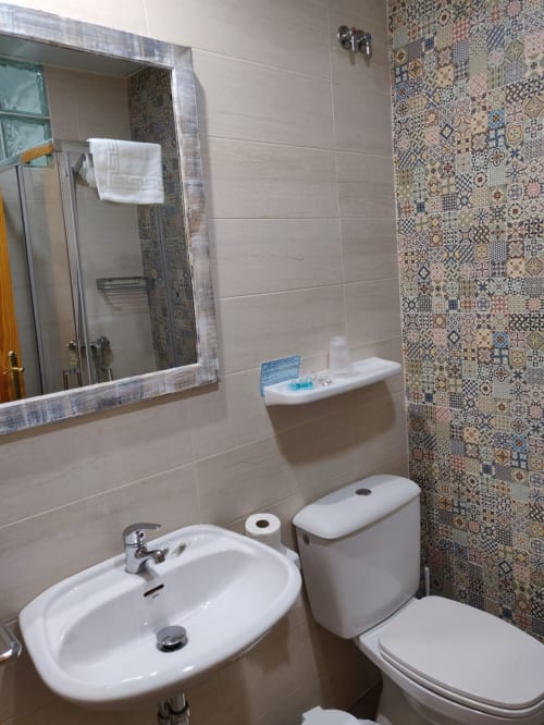 Baño moderno del Hotel La Posada con lavabo blanco, inodoro, espejo y pared de azulejos decorativos con patrón geométrico