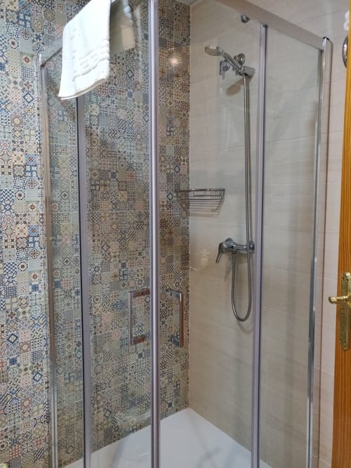 Moderno baño con azulejos decorativos, ducha de lluvia y puertas de cristal en Hotel La Posada