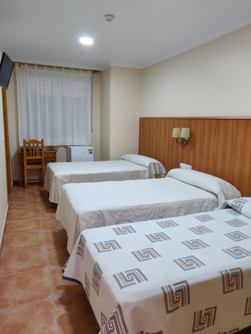 Habitación triple en Hotel La Posada con tres camas, cabecero de madera, escritorio, TV y ventana grande con cortinas
