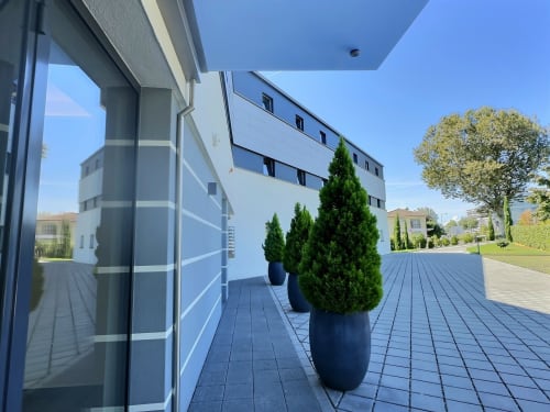 Terrasse moderne à Attica Résidences à St-Sulpice avec cyprès en pots, terrasse grise et bâtiment blanc contemporain