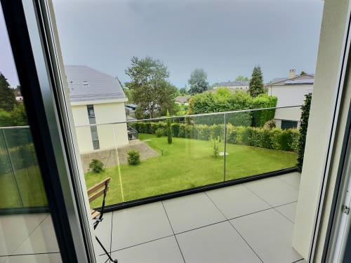 Balcon moderne avec balustrade en verre donnant sur un jardin verdoyant aux Résidences Attica, St-Sulpice