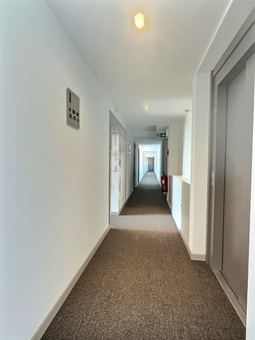 Couloir moderne d'Attica Résidences à St-Sulpice avec murs blancs, sol moquetté, portes numérotées, sortie de secours
