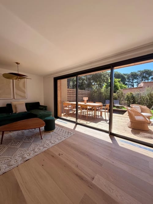 Salon de villa moderne avec canapé noir, table basse en bois et baies vitrées donnant sur terrasse aménagée