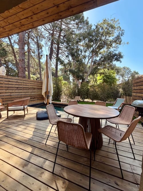 Terrasse en bois aux Villas d'A Storia à Porto-Vecchio avec table à manger, chaises en rotin, piscine et vue sur la forêt