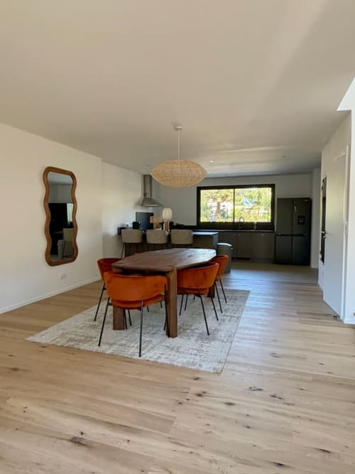 Salle à manger moderne avec chaises orange à table en bois, cuisine ouverte, suspension en osier, parquet en bois à Villa San