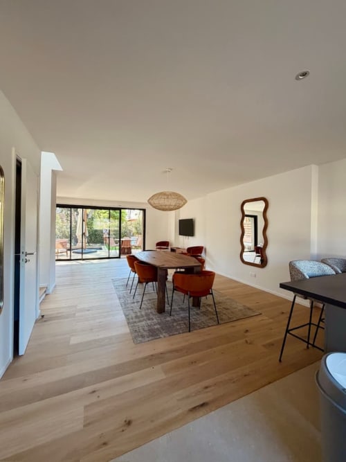 Salle à manger de villa moderne avec parquet, table de repas, chaises rouges et grandes portes coulissantes ouvrant sur la piscine