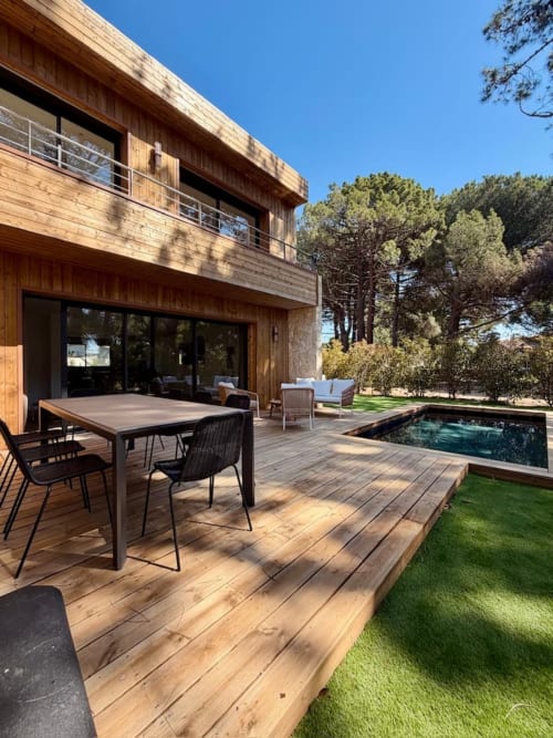 Patio de la Villa Cala Rossa avec terrasse en bois, table à manger, chaises longues et piscine privée donnant sur les pins