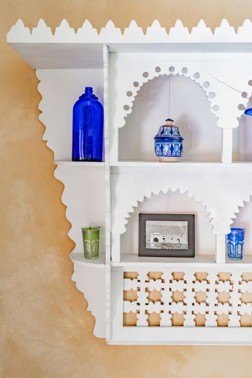 Étagères décoratives blanches présentant des bouteilles en verre bleu, des vases en céramique et des tableaux encadrés dans la chambre L'Étang du Moulin de
