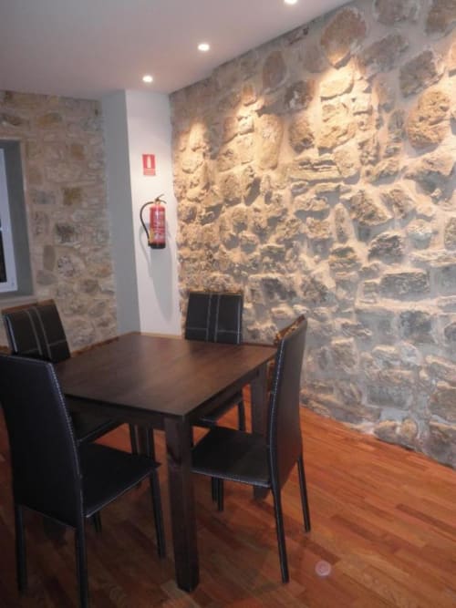 Comedor del Hostal Doña Blanca con muros de piedra, mesa de madera, sillas negras e iluminación moderna