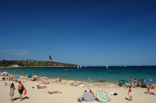 Journée animée à Sainte-Lucie-de-Porto-Vecchio : baigneurs, voiliers et kite-surfeur dans les eaux turquoise