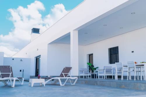 Terraza blanca moderna en Barrosa Home con tumbonas, comedor y vista al mar bajo cielo azul