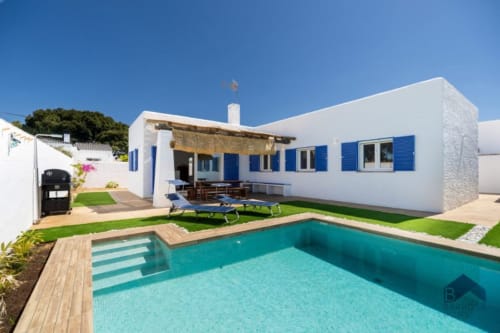 Villa moderna blanca en España con persianas azules, piscina turquesa, tumbonas y jardines cuidados
