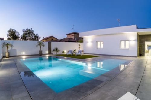 Piscina de lujo Barrosa al atardecer con edificio moderno blanco iluminado y jardín en España
