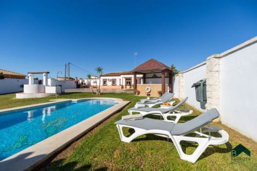 Villa Barrosa con piscina, tumbonas y jardines cuidados bajo un cielo azul despejado
