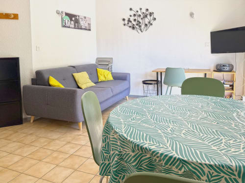 Studio LOCADIGNE à Digne-les-Bains avec canapé gris, coin repas, lit couverture motifs verts et TV