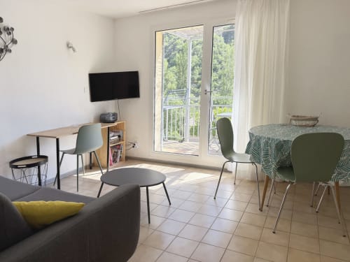 Salon moderne de LOCADIGNE avec télévision, portes donnant sur un balcon avec vue sur les montagnes, salle à manger et mobilier confortable