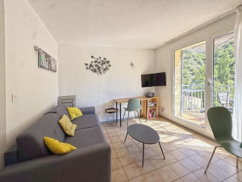 Séjour moderne avec canapé gris, coussins jaunes, bureau et vue montagne depuis le balcon de LOCADIGNE