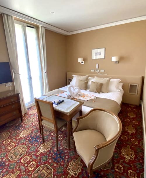 Camera standard dell'Hotel Splendid Cannes con pareti beige, letto queen, scrivania in legno, poltrona e tappeto a motivi rossi