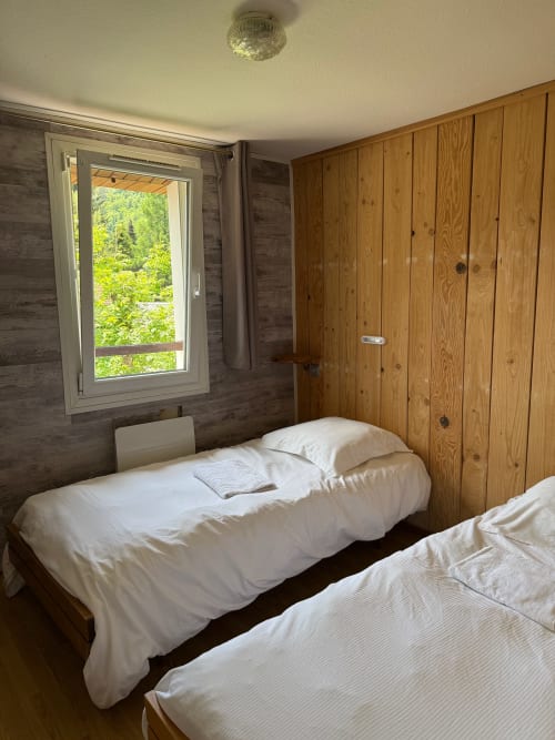Chambre chaleureuse du Chalet Cossu avec lits jumeaux, boiseries et vue sur le jardin aux Grandes Voies