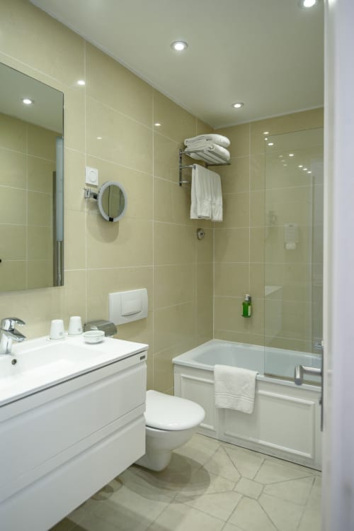 Bagno moderno con piastrelle giallo pallido, sanitari bianchi, doccia in vetro e servizi all'Hotel Splendid Cannes