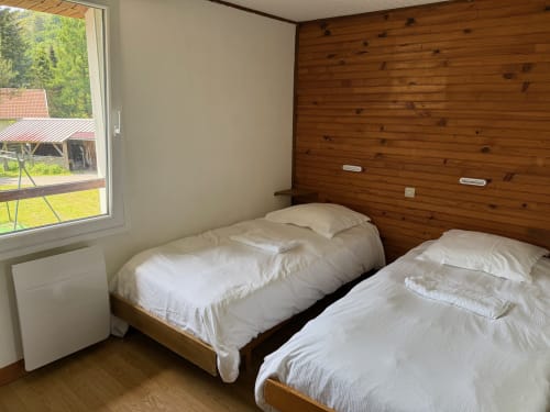 Lits jumeaux aux draps blancs dans la chambre d'un chalet en bois aux Gîtes les Grandes voies, Le Ménil, avec vue sur le jardin