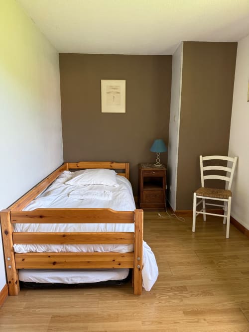 Chambre confortable du Chalet Cossu avec lit en bois, mur d'accent marron, fauteuil blanc et parquet aux Gîtes les Grandes voies