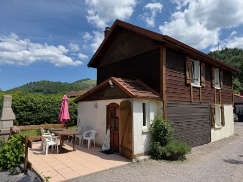 Cottage Chalet Cossu aux Gîtes les Grandes voies à Le Ménil avec terrasse-jardin, parasol rose et vue montagne