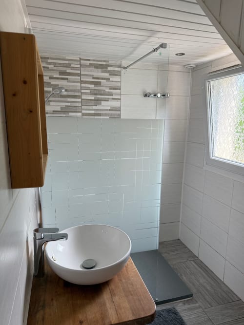 Salle de bain moderne du Chalet Cossu avec douche en carrelage blanc, vasque ronde sur meuble en bois et vue sur le jardin