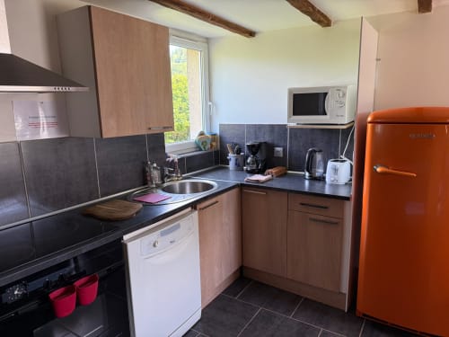 Cuisine de gîte avec réfrigérateur orange rétro, plan de travail foncé, meubles en bois, micro-ondes et vue sur le jardin