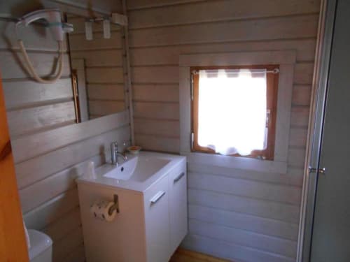 Salle de bain moderne du chalet Les Chalets de Lozzi avec lavabo blanc, toilettes et baie lumineuse donnant sur le lac de Calacuccia