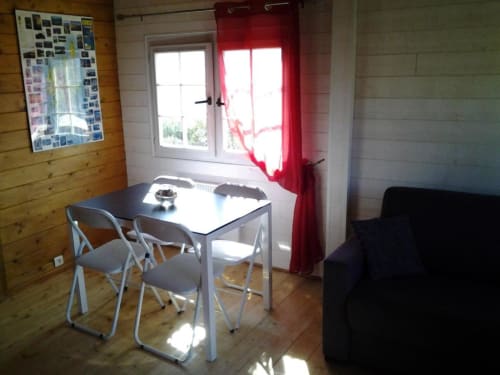 Salle à manger lumineuse du Chalet Deux Chambres aux Chalets de Lozzi, Calacuccia, avec table, chaises, rideaux rouges et vue sur le lac