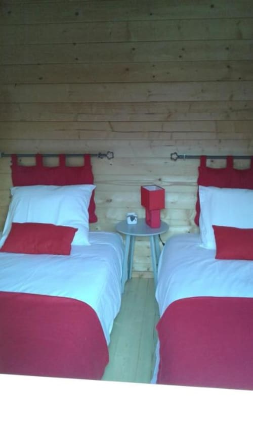 Lits jumeaux aux draps rouge et blanc dans une chambre de chalet en bois aux Chalets de Lozzi, Calacuccia