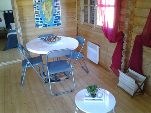 Intérieur de chalet en bois avec tables rondes blanches, chaises bleues, rideaux bordeaux et parquet aux Chalets de Lozzi