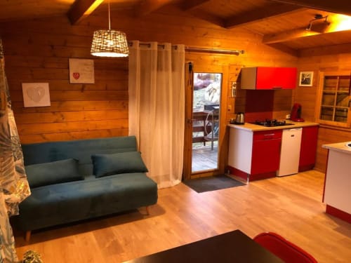 Intérieur cosy de chalet en bois avec canapé vert, cuisine rouge et blanche, parquet et vue sur le lac aux Chalets de