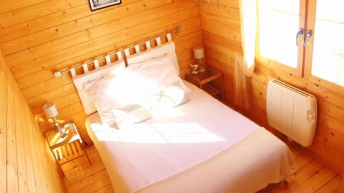 Chambre cosy aux murs en pin des Chalets de Lozzi, avec literie blanche et lumière naturelle par la fenêtre