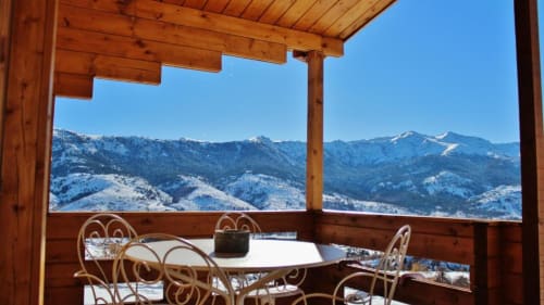 Terrasse de chalet en bois avec table de salle à manger face aux montagnes enneigées aux Chalets de Lozzi, Calacuccia